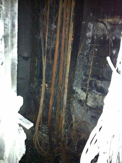 Một chiến sĩ CS PCCC tham gia làm nhiệm vụ (ảnh trái); Những đường dây điện trong hộp kỹ thuật cháy đen (ảnh phải)