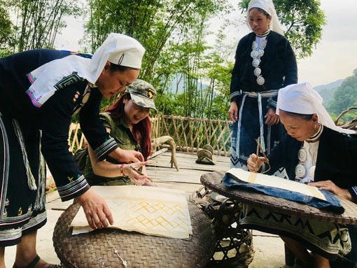 Những người phụ nữ dân tộc Dao Tiền nhiệt thành hướng dẫn
cách vẽ và in sáp ong cho du khách. (Ảnh: Bảo Châu)