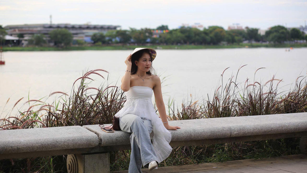 Du khách tạo dáng chụp ảnh bên bờ sông Hương, giữa những bông cỏ lau đang nở rộ, tận hưởng khung cảnh dịu dàng của mùa cuối hạ.