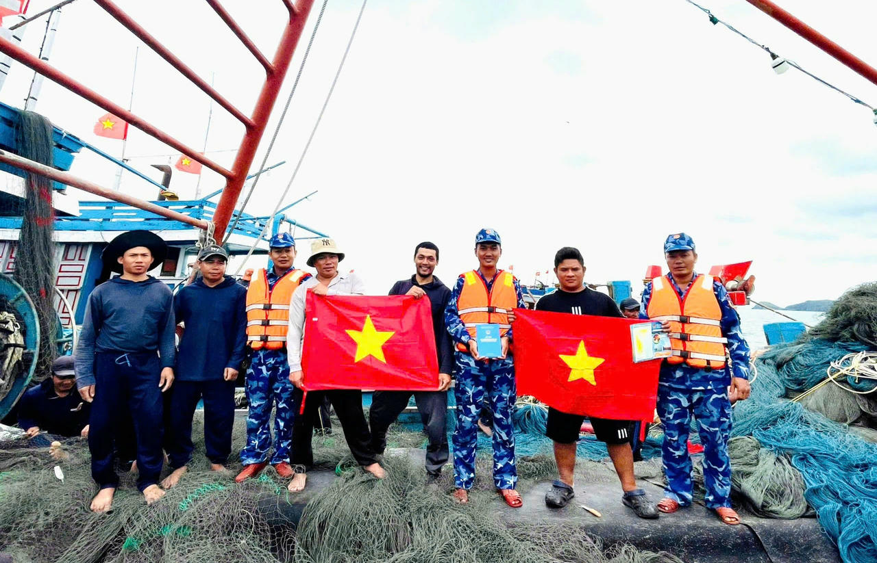 Tổ công tác của Cảnh sát biển phát tờ rơi tuyên truyền và tặng cờ Tổ quốc cho ngư dân trên tàu cá QB-91149-TS.