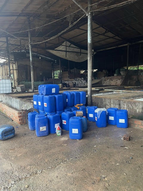 Thùng nhựa xanh chứa hóa chất tập kết ngổn ngang trong khuôn viên một xưởng, không có biện pháp che chắn hay xử lý an toàn. 