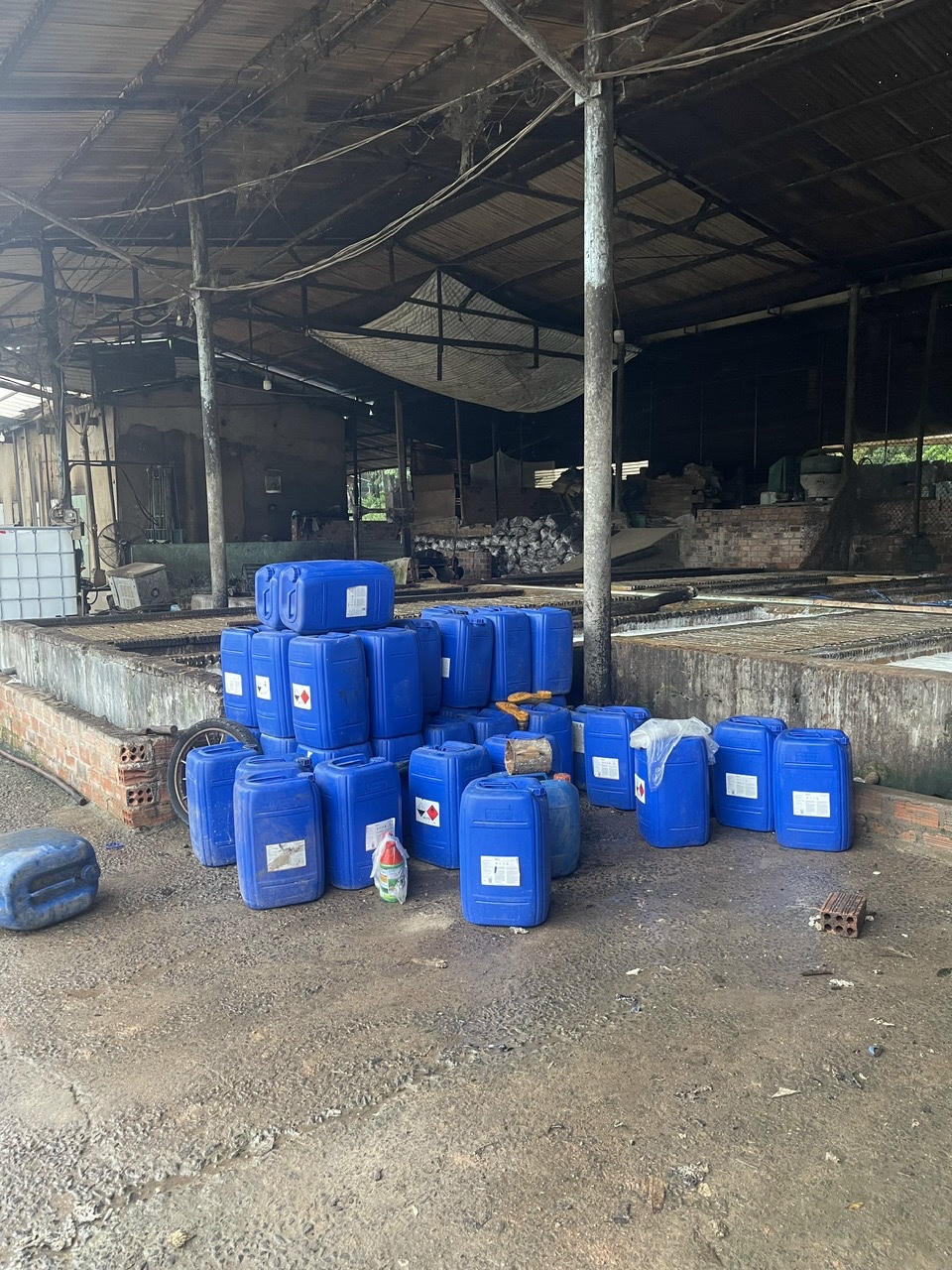 Hàng chục thùng nhựa xanh chứa hóa chất tập kết ngổn ngang trong khuôn viên xưởng, không có biện pháp che chắn bảo quản an toàn. 