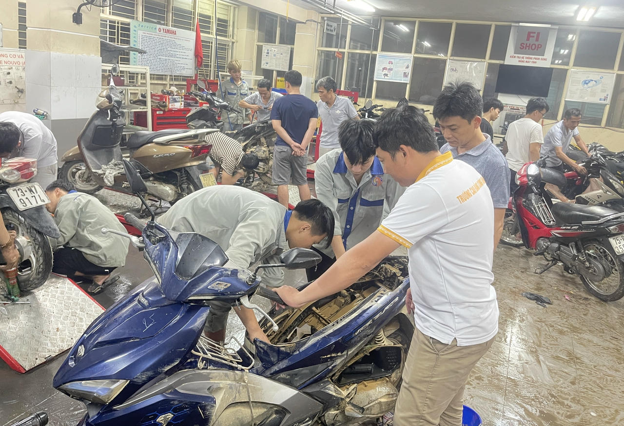 Thầy Thế Anh (áo sáng màu) hướng dẫn sinh viên sửa chiếc xe bị ngâm lũ hư hỏng nặng nề.