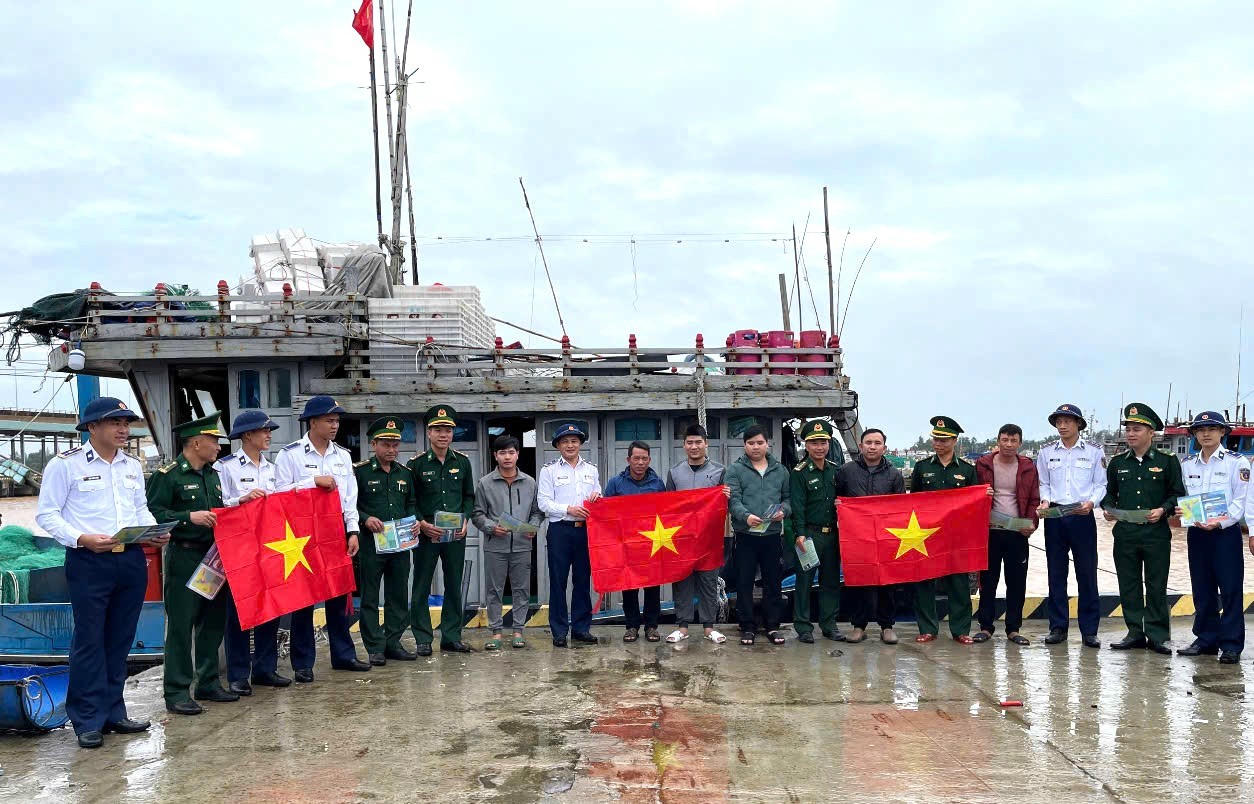Cán bộ Biên phòng và Cảnh sát biển trao cờ Tổ quốc và tài liệu pháp luật, động viên ngư dân chấp hành quy định IUU, vươn khơi an toàn.