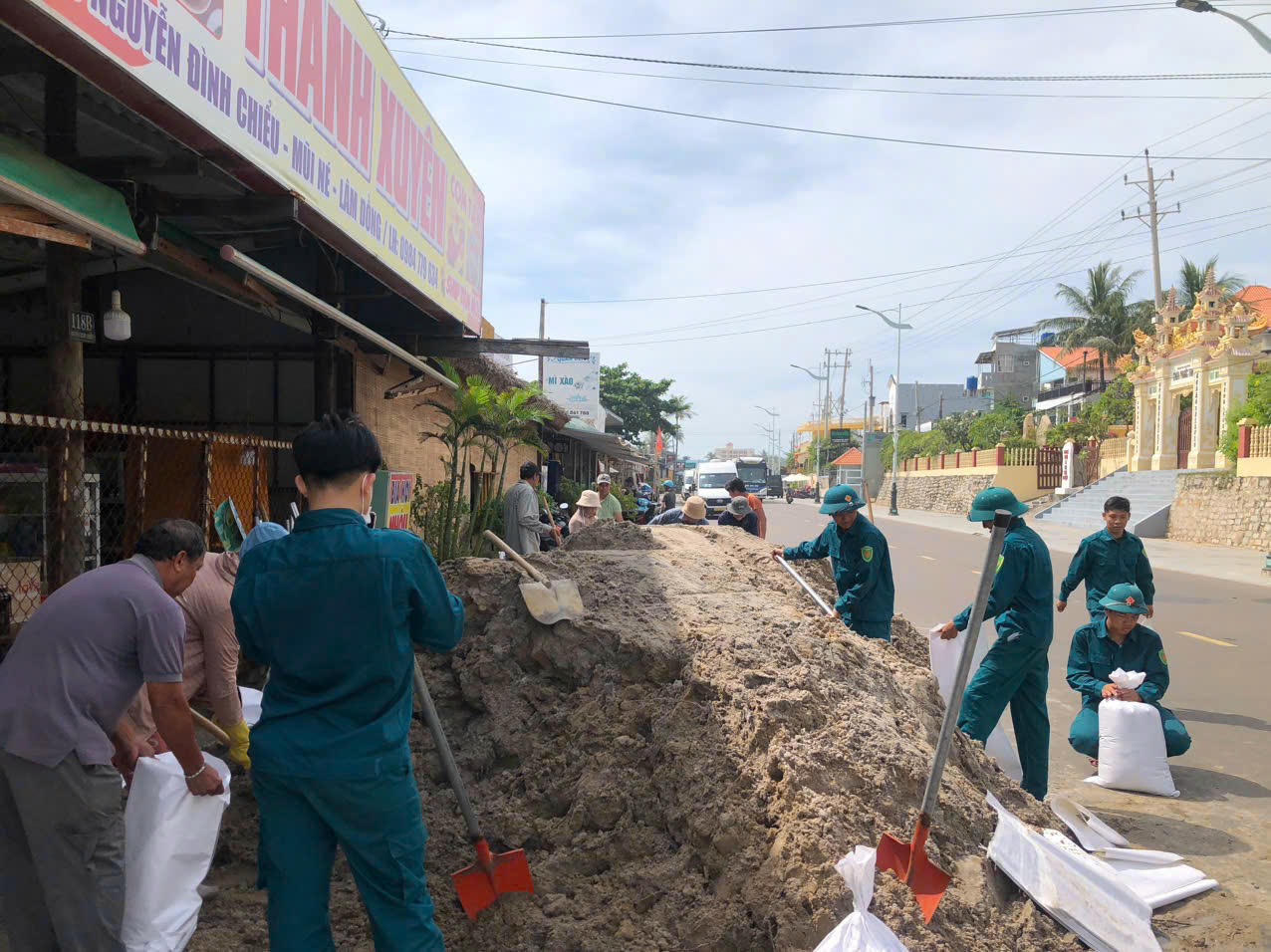 Lực lượng chức năng cùng người dân sử dụng bao cát gia cố bờ kè bị sạt lở.