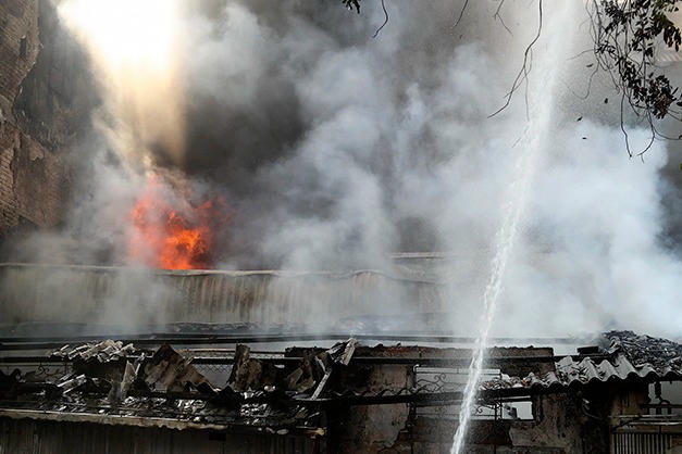 Lực lượng PCCC phun nước trực diện vào khu vực đang cháy, khói trắng dày đặc phủ kín cả dãy nhà. (Ảnh: TTXVN).