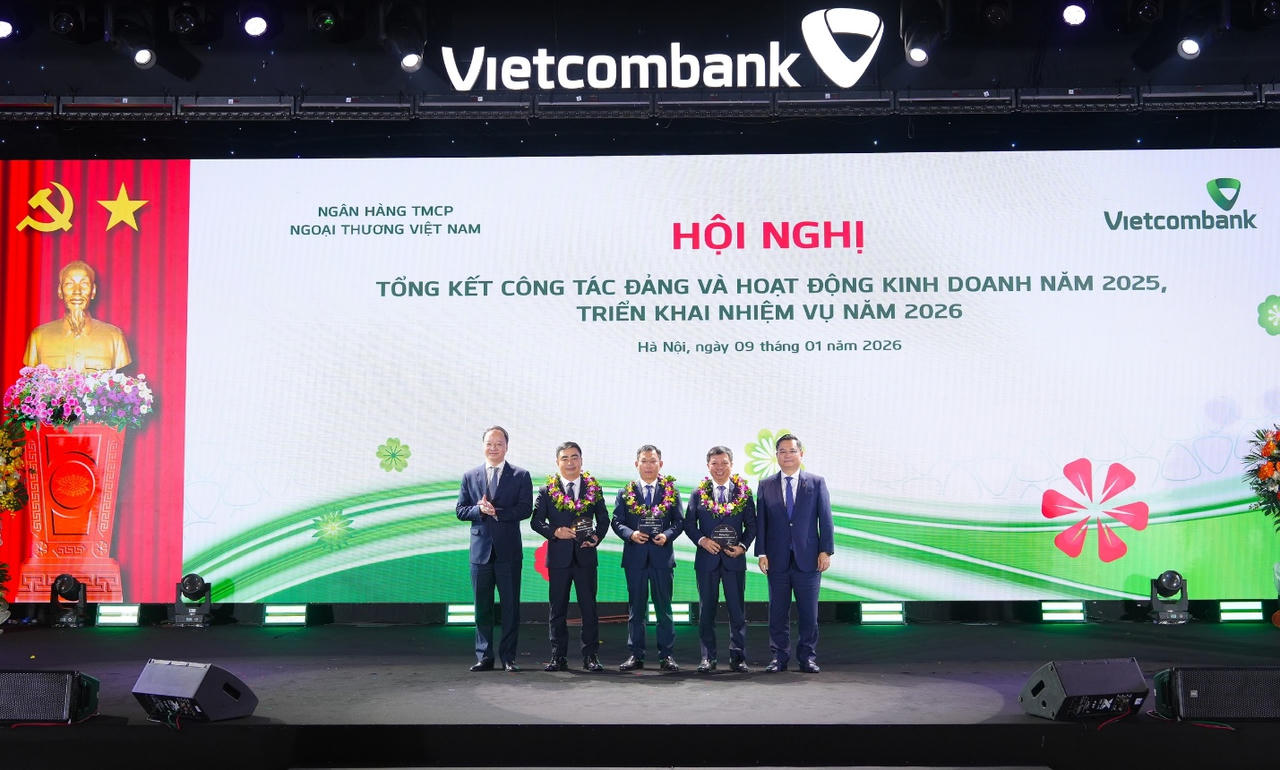 Đồng chí Nguyễn Thanh Tùng - Ủy viên BCH Đảng bộ Chính phủ, Bí thư Đảng ủy, Chủ tịch HĐQT Vietcombank (ngoài cùng bên phải) và đồng chí Lê Quang Vinh - Phó Bí thư Đảng ủy, Thành viên HĐQT, Tổng Giám đốc Vietcombank (ngoài cùng bên trái) trao biểu trưng và tặng hoa vinh danh cho đại diện 03 đơn vị hoàn thành đặc biệt xuất sắc nhiệm vụ kinh doanh năm 2025 gồm Vietcombank Sở giao dịch, Vietcombank Nam Sài Gòn, Vietcombank Thành Công