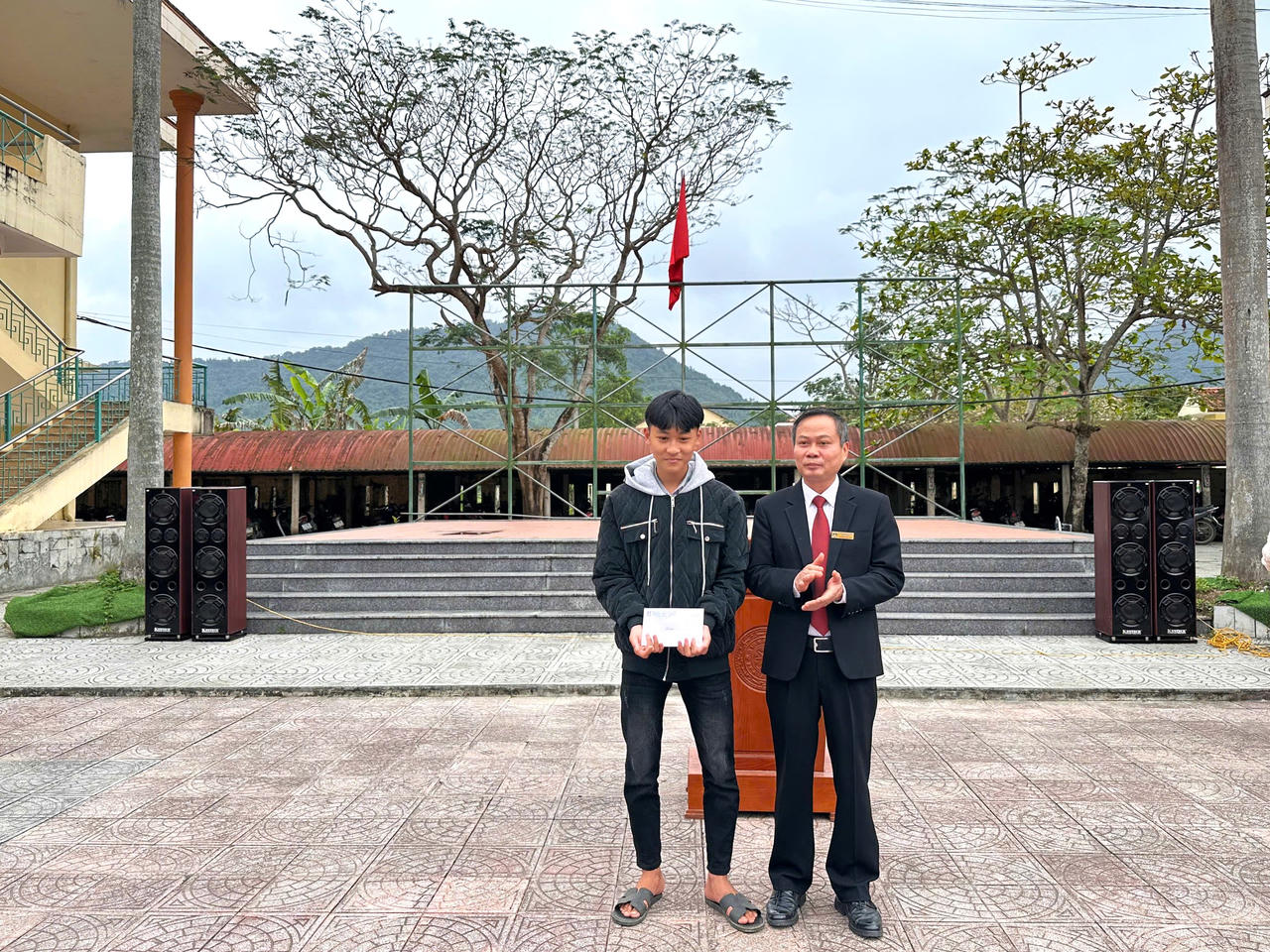 Thầy Nguyễn Minh Đức, hiệu trưởng nhà trường tuyên dương và trao thưởng cho em Cao Hoàng Ân Đức vì hành động dũng cảm cứu người trên sông Gianh.