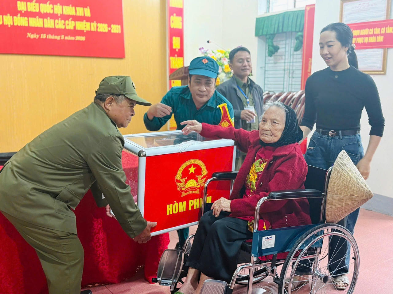 Thành viên tổ bầu cử giúp đỡ cử tri già cả đi lại khó khăn tham gia bỏ phiếu thực hiện quyền công dân của mình.