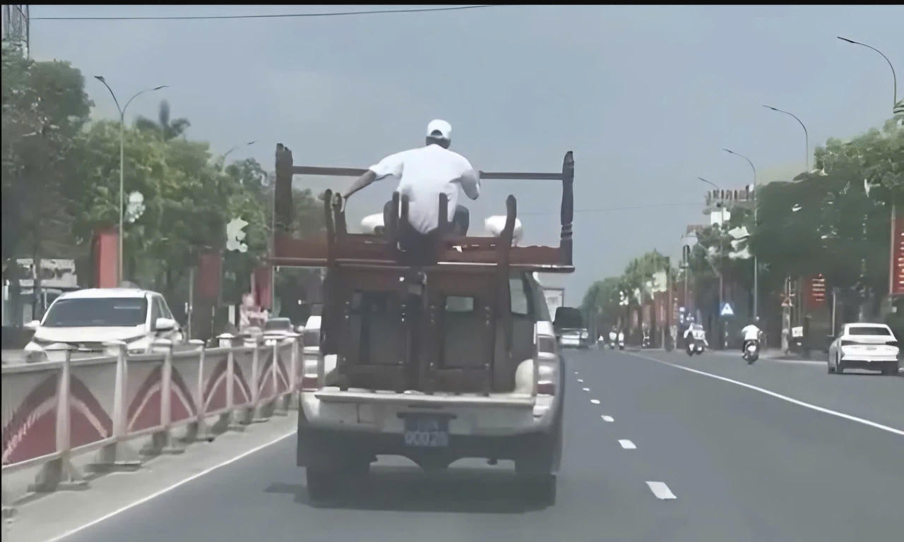 Hình ảnh ghi cảnh ô tô bán tải mang biển số xanh 75M-000.25 chở theo 4 cái bàn, 4 cái ghế và người ngồi phía sau thùng.