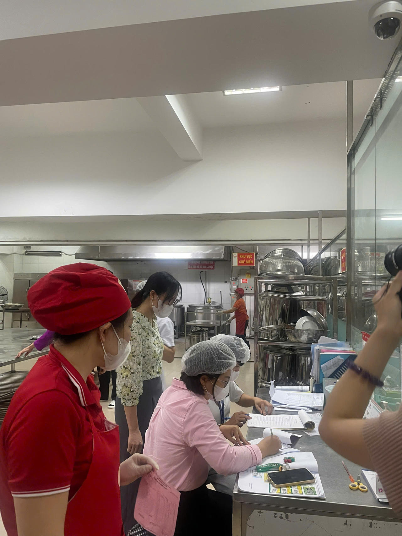 Lực lượng chức năng đối chiếu hồ sơ, sổ sách, biểu mẫu kiểm thực và các tài liệu liên quan trong quá trình kiểm tra đột xuất bếp ăn nhà trường.