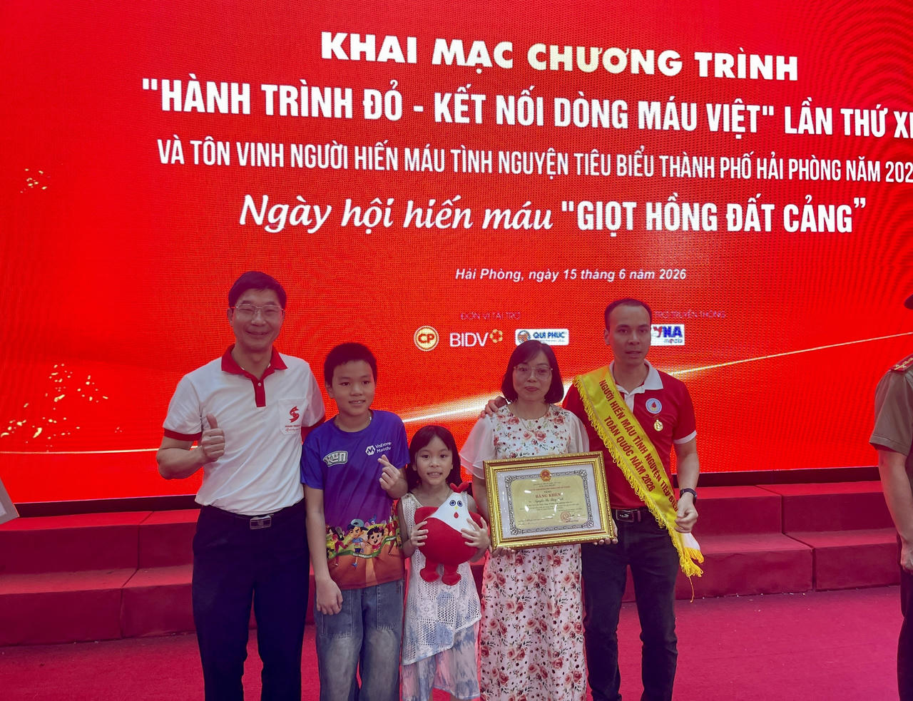 PGS.TS.BS Trần Ngọc Quế - Phó Trưởng ban Tổ chức Hành trình đỏ, Giám đốc Trung tâm Máu quốc gia, chụp ảnh lưu niệm cùng gia đình anh Bùi Đức Toàn - người đã hiến máu và thành phần máu tổng số 68 lần.