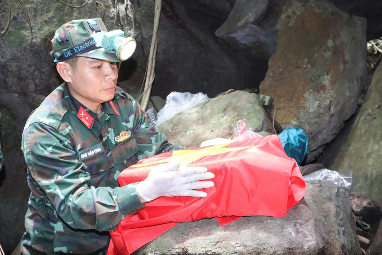 Trưa 13/7, bộ hài cốt liệt sĩ đầu tiên được phủ cờ Tổ quốc để bộ đội đưa ra bên ngoài. (Ảnh: Vân Anh)