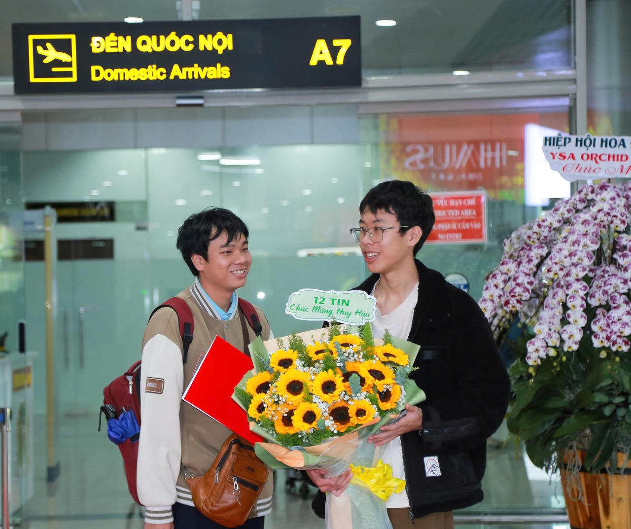Bạn bè tặng hoa, chúc mừng em Đặng Huy Hậu trở về sau khi xuất sắc giành Huy chương Bạc tại Kỳ thi Olympic Tin học Quốc tế (IOI) năm 2026. (Ảnh Sở GD&ĐT Lâm Đồng)