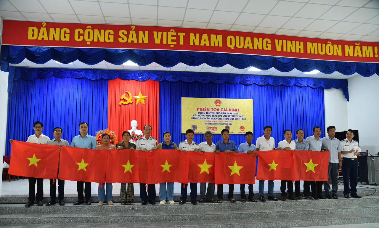 Đại diện BTL Vùng Cảnh sát biển 4, lãnh đạo địa phương và các đại biểu trao tặng Cờ Tổ quốc cho ngư dân tham dự "phiên tòa giả định". Ảnh: Quang Vinh