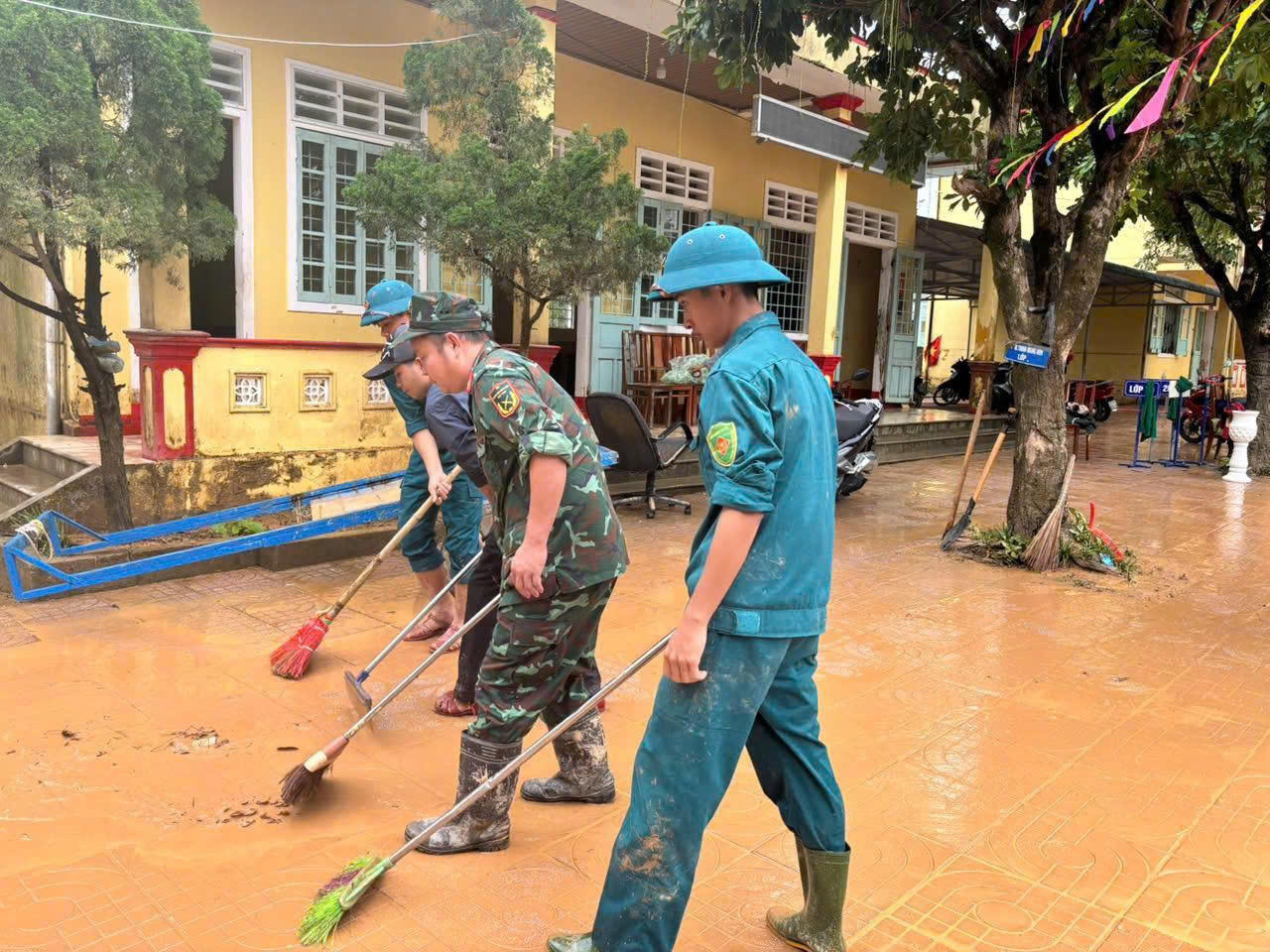 Cán bộ, chiến sĩ lực lượng vũ trang giúp vệ sinh, dọn dẹp khuôn viên trường học sau ngập lụt. (Ảnh: X.D)