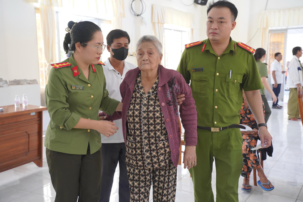 Cán bộ Công an xã Tân Tiến hỗ trợ thân nhân liệt sĩ cao tuổi, sức khỏe yếu đến điểm thu nhận mẫu sinh phẩm ADN (Ảnh: H.Đ).