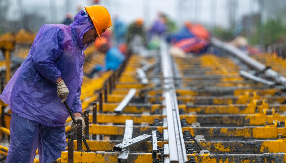 Công nhân đội mưa thi công hạng mục ray tuyến tàu điện nhẹ LRT, trong bối cảnh các công trường phục vụ APEC 2027 tại Phú Quốc đồng loạt chạy đua với thời tiết và tiến độ.