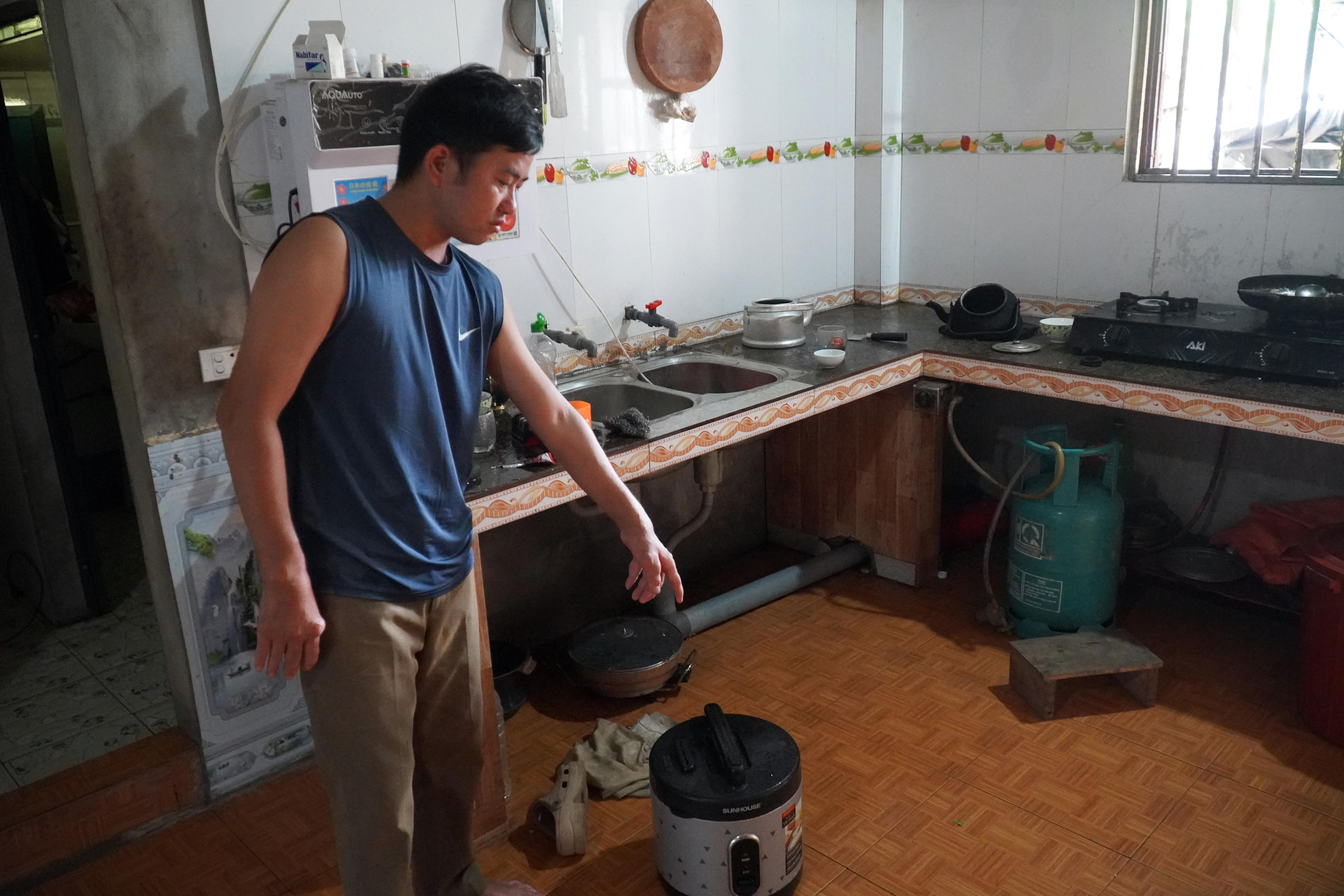 Ông Chảo Văn Hinh chỉ chỗ nước dột từ mái xuống và cho biết chân ông Hinh bị ghẻ do sống lâu ngày với nước bẩn.