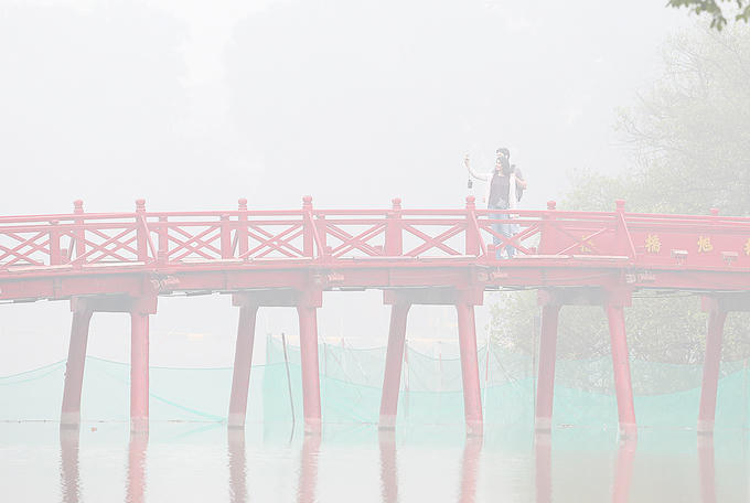 Khách du lịch dậy sớm chụp hình lưu niệm trên cầu Thê Húc trong màn sương mờ ảo.