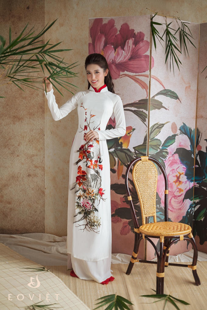 Thiết kế áo dài trắng cổ cao nhưng vẫn không hề cứng và đơn điệu bởi họa tiết chim công và hoa nổi bật trên nền trắng.