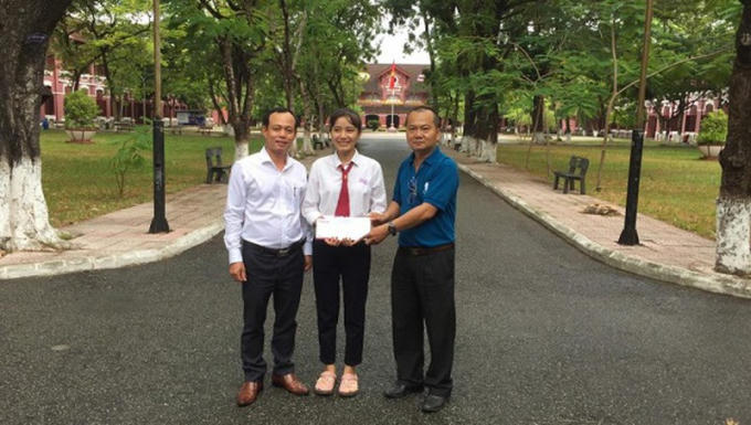 Nhà báo Nguyễn Quang Tám - Trưởng Văn phòng Đại diện Báo PLVN khu vực Bình Trị Thiên (trái) trao số tiền bạn đọc ủng hộ em Nhung.
