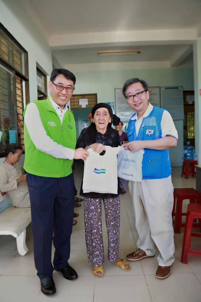 Tổng Giám đốc Doosan Vina Yeon In Jung (trái) và ông Kwon Jeong Taik, Giáo sư, bác sĩ khoa Phẫu thuật thần kinh, bệnh viện Chung Ang (phải) trao thuốc và quà cho một người dân.