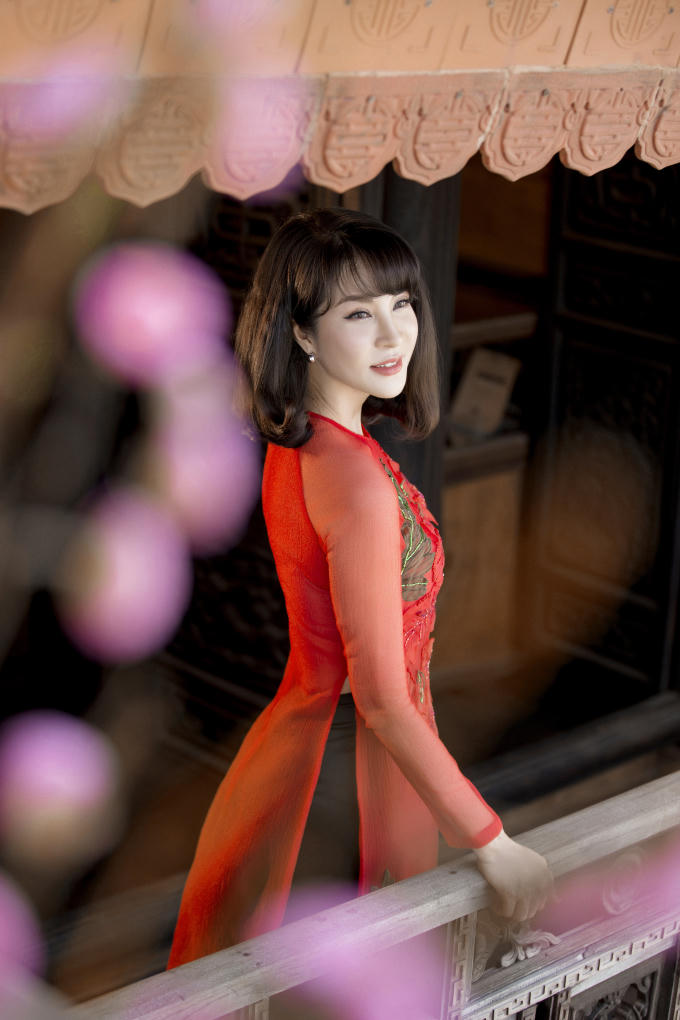 MC Thanh Mai nổi bật trong một mẫu áo dài gam màu hồng với nhiều họa tiết lạ mắt. Thiết kế cổ trụ truyền thống được thay bằng cổ tròn phóng khoáng. Phom dáng cũng trở nên rộng rãi và thoải mái hơn nhờ lược bỏ những đường chiết eo. Vì áo dài vốn đã rực rỡ nên Thanh Mai chọn lối trang điểm nhẹ nhàng, tiết chế phụ kiện, trang sức đi kèm.