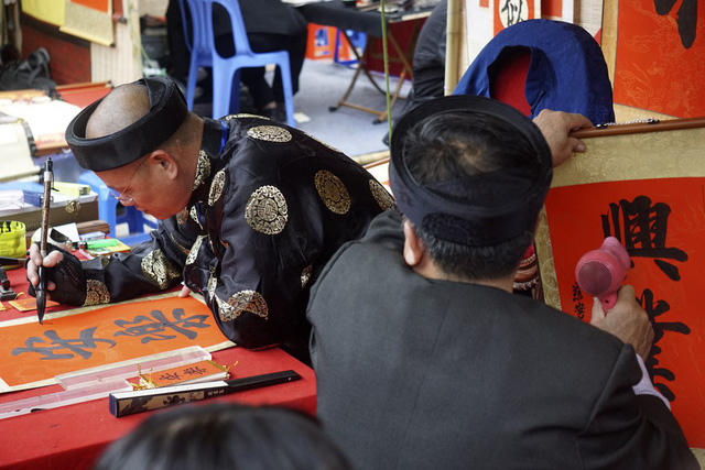 Ông đồ say sưa viết chữ, trong khi "đồng nghiệp" đang dùng máy sấy hong khô tác phẩm đã hoàn thành.