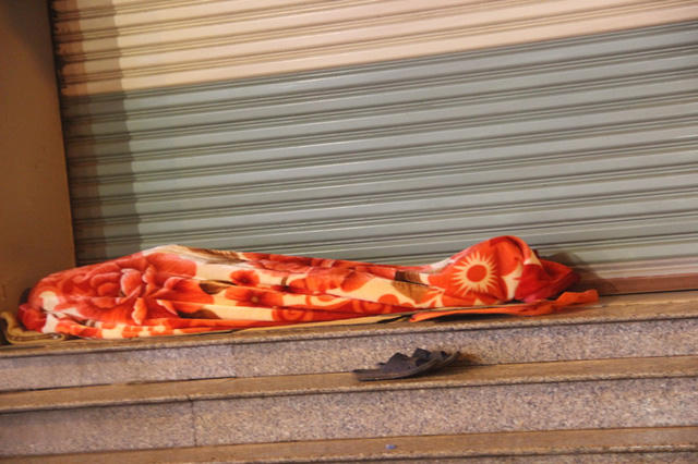 Một người tìm cho mình giấc ngủ cạnh quầy hàng, bên hành lang đường phố.