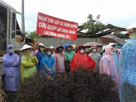 Những công nhân mặc áo mưa đội nón biểu tình đòi chế độ di dời theo quyết đinh. Ảnh: Như Trường.