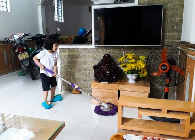 Bé Vũ Khánh Ly cầm chổi lau nhà, giúp đỡ cha mẹ (Ảnh: nhân vật cung cấp).
