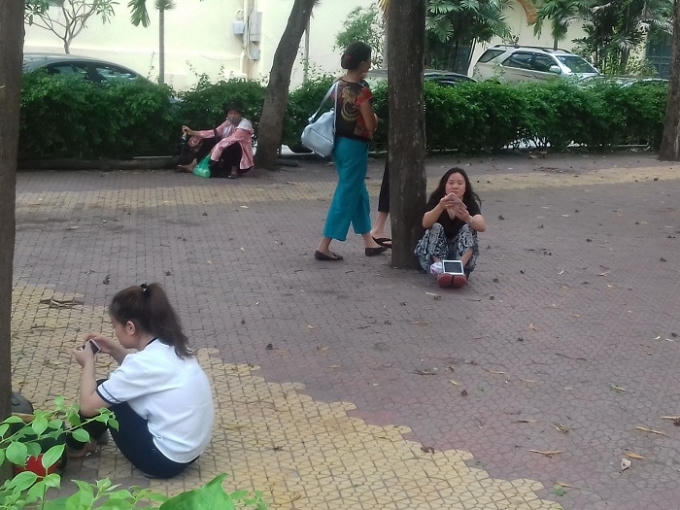 Phụ huynh ngồi dưới gốc cây để tránh nắng và đợi con em mình hoàn thành bài thi.