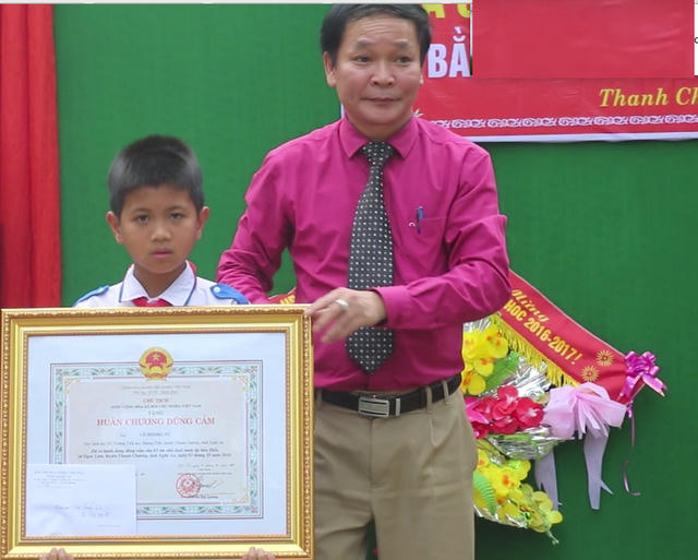 Ông Nguyễn Thanh Nhàn, phó Giám đốc Sở Nội vụ - Trưởng ban thi đua khen thưởng tỉnh Nghệ An ủy quyền Chủ tịch nước và Bộ GĐ-ĐT trao Huân chương dũng cảm cho em Tú. (Ảnh: Dân trí)
