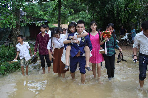 Chú rể sắn quần tới đầu gối, lội nước cõng cô dâu vượt qua dòng nước. Ảnh: Facebook