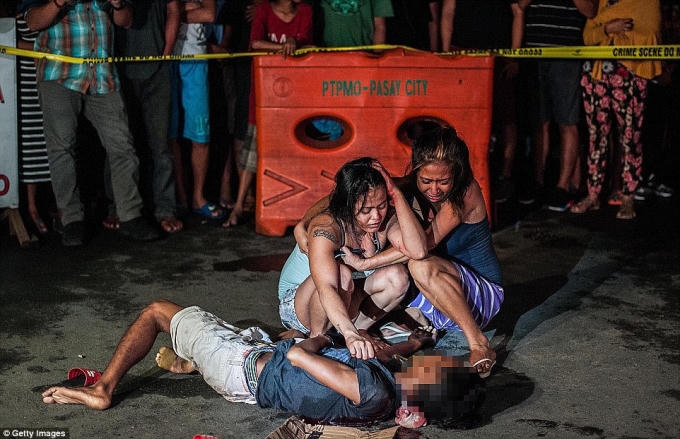 Một người vợ khóc bên xác chồng. Cô cho rằng chồng mình chỉ là 1 người đạp xích lô kiếm sống trong khi cảnh sát khẳng định đây là 1 tội phạm buôn ma túy. (Ảnh: Daily Mail)