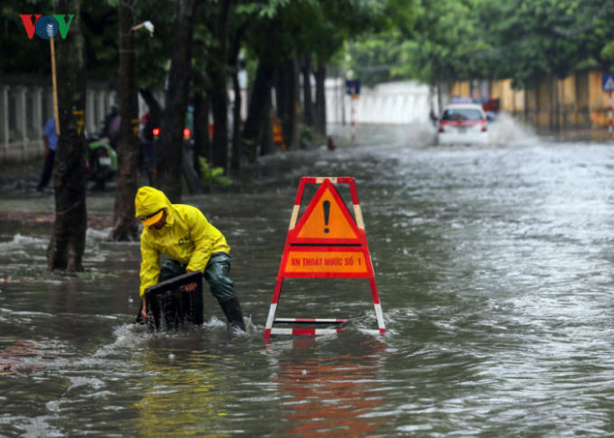 Một công nhân công ty thoát nước Hà Nội phải mở miệng cống để nước rút nhanh, tránh ngập úng kéo dài trên phố Thụy Khuê. (Ảnh:VOV)