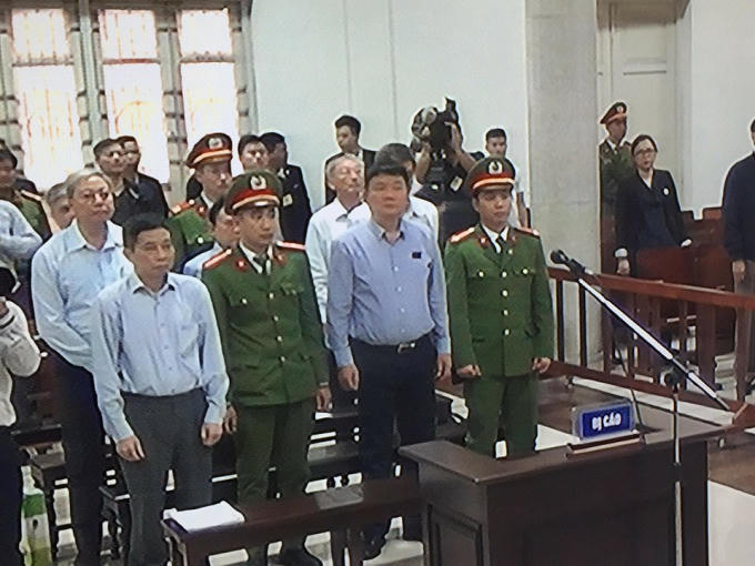 Bên trong phòng xử án, ông Đinh La Thăng mặc áo sơ mi sáng màu ngồi hàng ghế đầu cùng Ninh Văn Quỳnh.