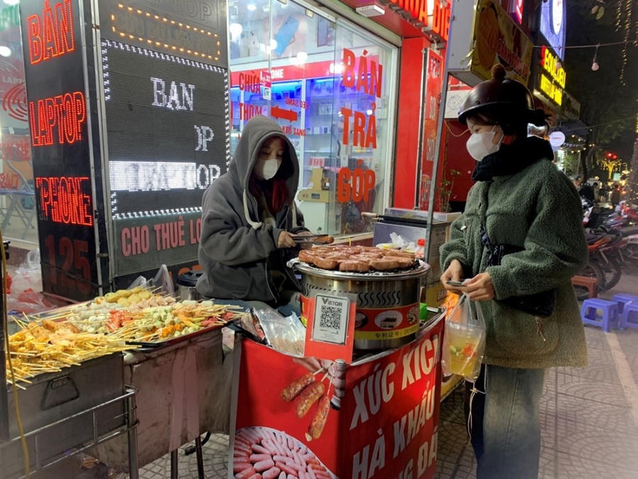 Những chiếc lạp xưởng thơm ngon được đem nướng trên một lớp đá sỏi, phía dưới là chiếc bếp điện để tạo nhiệt làm nóng.