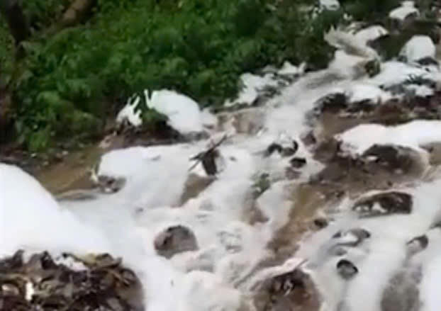 Dòng nước nổi bọt trắng chảy từ đồi Con Heo xuống khu dân cư.