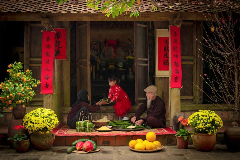 Hình ảnh các cụ già ngồi bên hiên nhà cùng cháu nhỏ gói bánh chưng giữa không gian nhuốm màu thời gian của những ngôi nhà trăm năm tuổi lay động người xem.