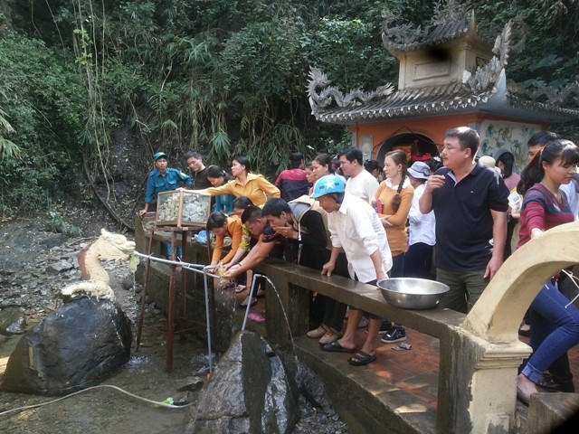 Bất chấp cái lạnh, nhiều du khách rửa mặt từ vòi nước dẫn từ chân thác "nước thánh" về, với mong muốn sẽ gặp nhiều may mắn. Những du khách khác thì chen nhau hứng nước từ dòng thác vào chai, với mong muốn lấy lộc đầu Xuân. (Ảnh: A.Thắng)