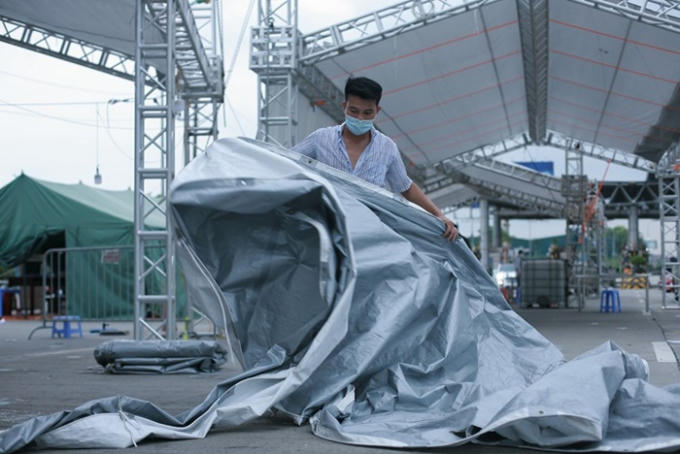 Một người thợ đang khẩn trương căng lại bạt phủ lán tại chốt kiểm soát dịch bệnh Covid-19 Pháp Vân - Cầu Giẽ trước cơn dông chiều tối 12/8.
