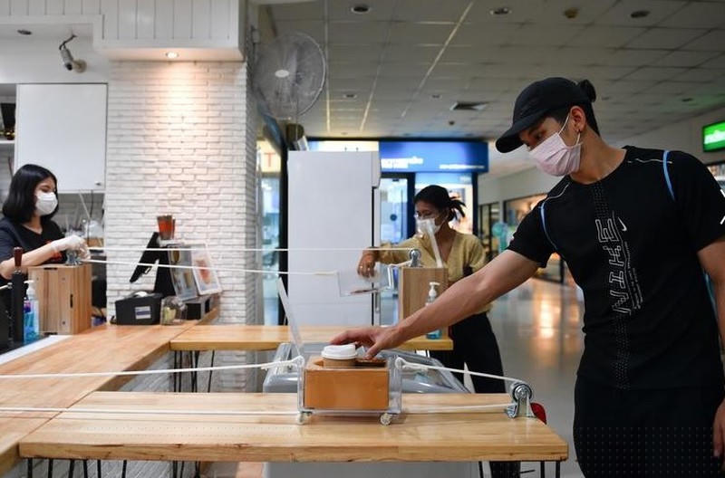 Một người đàn ông nhận cà phê trong xe kéo bằng dây thừng trong một quán cà phê áp dụng chính sách “khoảng cách xã hội” cho khách hàng của họ ở Bangkok, Thái Lan.