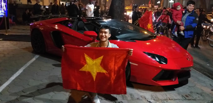 Một chiếc siêu xe màu đỏ trên phố Hai Bà Trưng, Hà Nội được người hâm mộ vây quanh chụp ảnh lưu niệm.