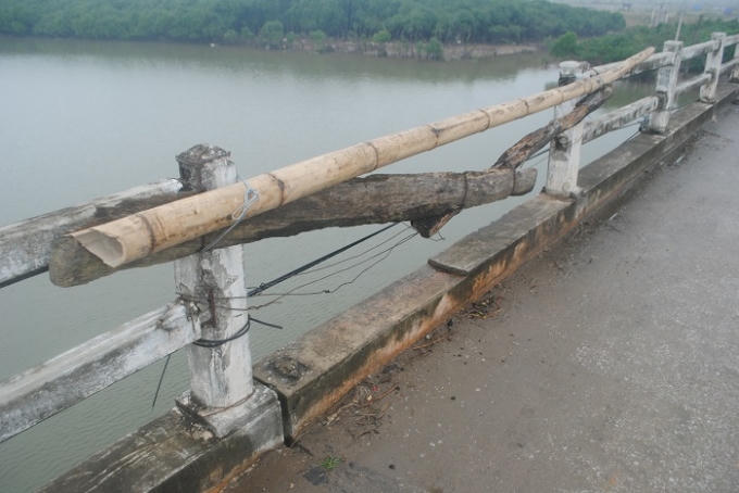 Cọc tre, nứa và thân gỗ được cột tạm bợ để níu lan can cầu. (Ảnh: Duy Ngợi).