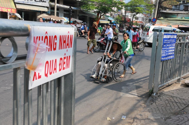 Bà Nguyễn Thị Thiện (73 tuổi) đi xe lăn bán vé số. Trước kia bà có thể lên lề đi vòng quanh vỉa hè bán. Nhưng từ ngày lắp rào chắn, bà buộc phải bán hàng dưới lòng đường.