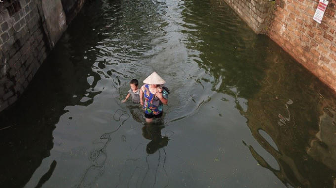 Người già và trẻ nhỏ là người bị chịu ảnh hưởng nặng nề nhất trong trận ngập lụt lần này. Trên ảnh là hai bà cháu dắt nhau đi lánh nạn đi trên đường làng với dòng nước đen kịt ô nhiễm.