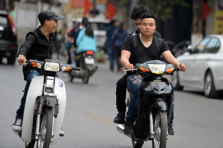 Thanh niên đội mũ mềm vừa đi vừa tán chuyện với người đi xe song song.