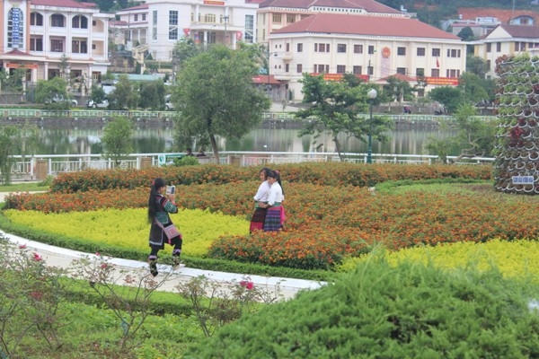 Những cô gái trong trang phục dân tộc đang tạo dáng chụp ảnh giữa vườn hoa.